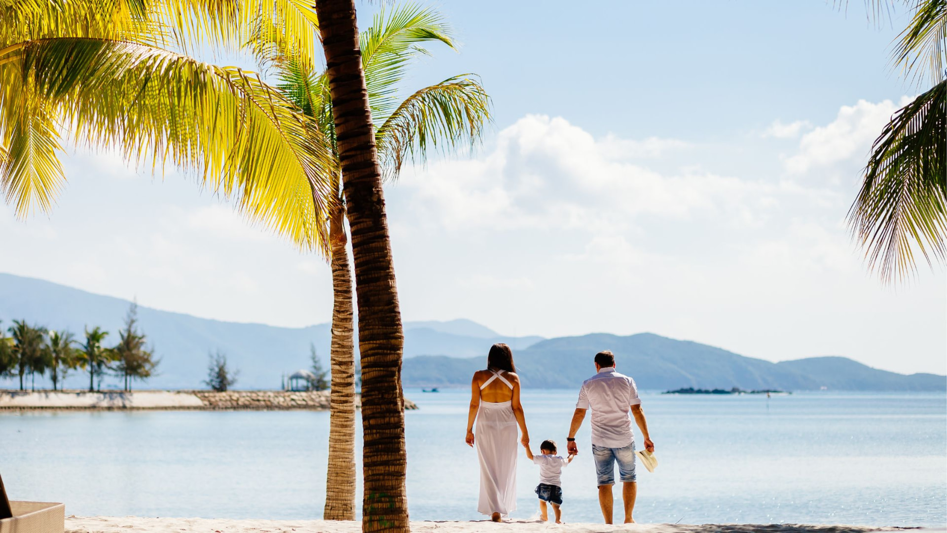 Family walking hand-in-hand on a beach under palm trees